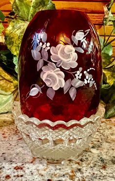 a glass vase with flowers painted on it sitting on a counter top next to plants