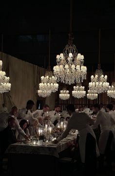 a group of people sitting around a table in a room with chandeliers hanging from the ceiling