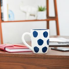 a blue and white polka dot coffee mug sitting on top of a desk next to a laptop