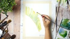 a person is holding a paintbrush and drawing on a piece of paper with watercolors