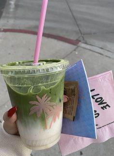 a person holding up a green drink with a pink straw