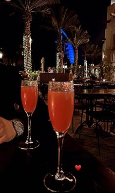 two wine glasses sitting on top of a table next to each other in front of palm trees