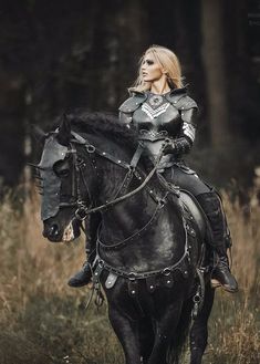 a woman in armor riding on the back of a black horse through a field with tall grass