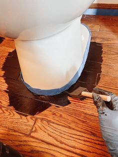 a white toilet sitting on top of a wooden floor next to a paint roller and brush