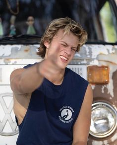 a woman pointing at the camera in front of an old van with her eyes closed