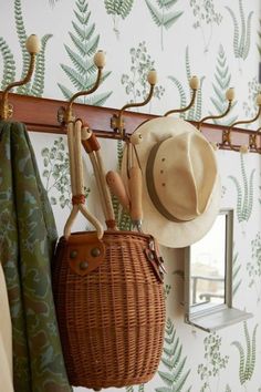 a basket with hats hanging from it next to a mirror and coat rack on the wall