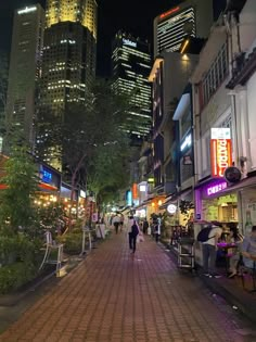 people are walking down the street in front of tall buildings at night with lights on