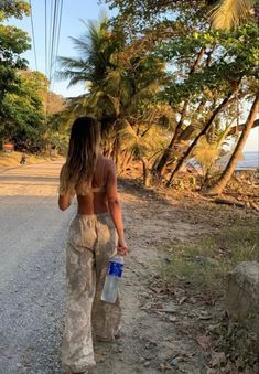 a woman walking down a dirt road with a water bottle in one hand and a cell phone in the other