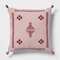 a pink and red embroidered pillow with tassels on the sides, sitting on a white surface