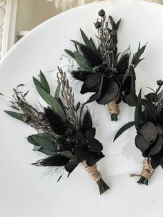 three black flowers on a white plate with green leaves and twine tied to them