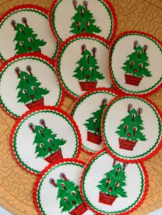 twelve embroidered christmas tree coasters in red and green on a tan placemat with white trim