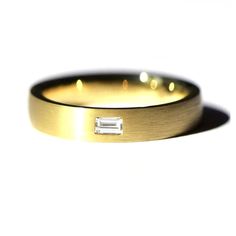 a gold wedding band with a baguette cut diamond in the center, against a white background