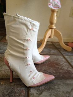 a pair of white high heeled shoes sitting on top of a tile floor next to a wooden stand