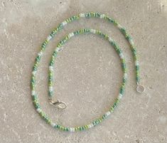 a green and white beaded necklace with a silver clasp on a stone surface,