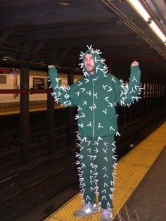 a man in a green outfit standing next to a train platform with his arms up