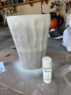 a spray can sitting on top of a table next to a cement vase and some other items