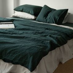 an unmade bed with green linens and pillows on the headboard, along with a book