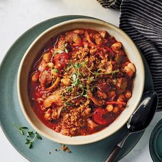 a bowl filled with meat and vegetables on top of a plate next to a spoon