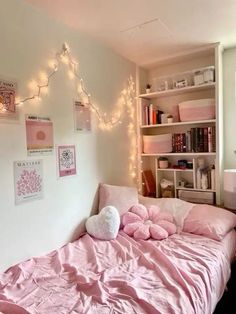 a bed with pink sheets and pillows in a room decorated with lights, bookshelves and pictures on the wall