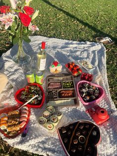 an outdoor picnic with food and drinks on the blanket in the grass, including cupcakes