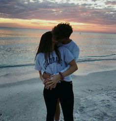 a man and woman kissing on the beach at sunset, with their arms around each other