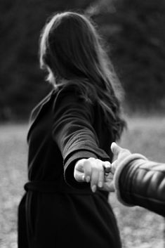 two people holding hands and walking through a field