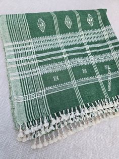 a green and white plaid blanket with tassels on the bottom, sitting on a bed