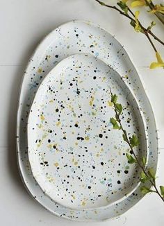 two white plates with black and yellow speckles on them next to some flowers