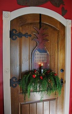 a wooden door with a pineapple wreath on top and candles in the center, surrounded by greenery