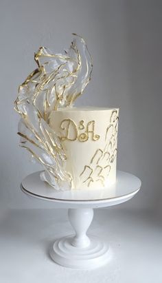 a white and gold wedding cake with swirls on top is sitting on a pedestal