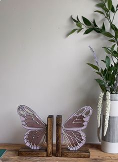 two butterfly figurines sitting next to each other on a wooden shelf near a vase with flowers