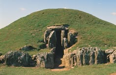 a large grassy hill covered in rocks and grass with a small cave at the top