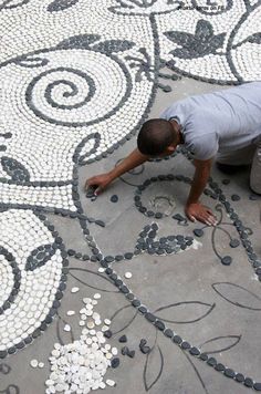 a man kneeling down on the ground working on a mosaic tile design that looks like flowers