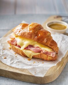 a ham and cheese croissant on a wooden cutting board next to dipping sauce