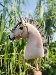 a close up of a toy horse on a stick in front of some grass and trees