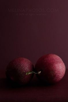 two red fruit sitting on top of a table next to each other in front of a purple background