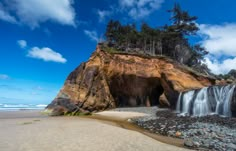 a waterfall cascading into the ocean next to a rocky cliff on a beach