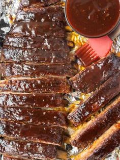 bbq ribs and barbecue sauce on tin foil with tongs next to the grill