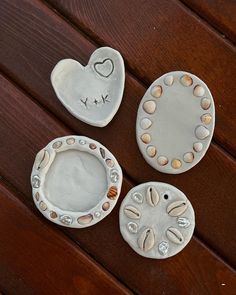 three ceramic dishes sitting on top of a wooden table next to each other with hearts and seashells painted on them