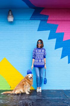 a woman standing in front of a colorful wall with a dog sitting next to her