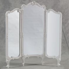 an ornately decorated white four - paneled mirror stands against a gray background in the shape of a room divider