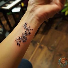 a woman's wrist tattoo with musical notes and flowers on the side of her arm