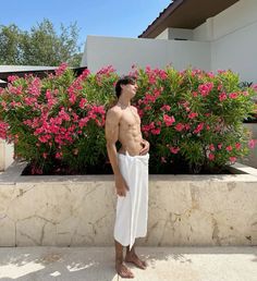 a shirtless man standing in front of some flowers