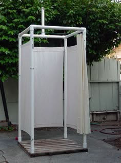 a white garment rack sitting on the side of a road next to a tree and fence