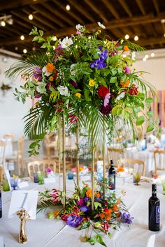 a tall vase filled with lots of colorful flowers on top of a white table cloth