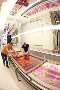 two men working on an art project in a large room with pink and orange designs