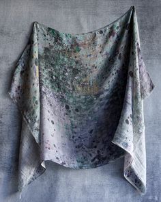 an artistically designed scarf hanging up on a gray wall with paint splatters all over it