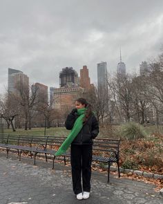 a woman standing in front of a park bench with a green scarf around her neck