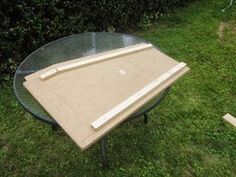 a table that is sitting in the grass near some bushes and trees, with two pieces of plywood on top