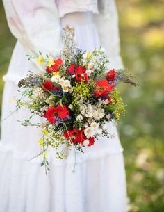 a woman in white dress holding a bouquet of flowers with red, yellow and white colors